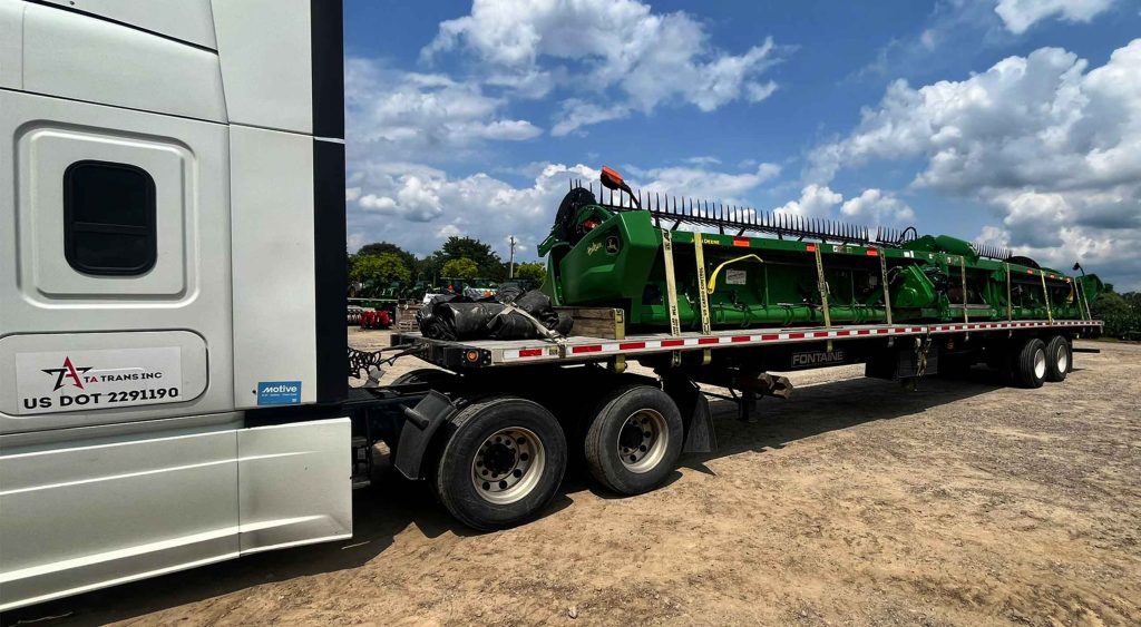 TA Trans Inc truck transporting large green agricultural machinery on a flatbed service trailer for a recent load.