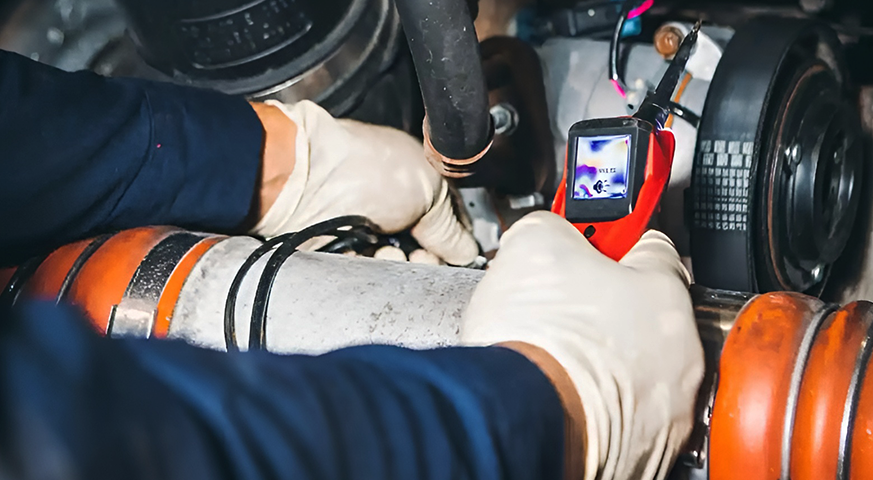 Technician using a thermal imaging camera to diagnose electrical issues in a semi-truck, highlighting repair insights.