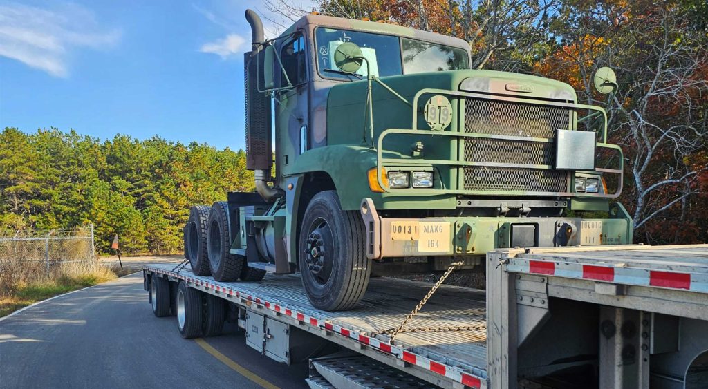 Military vehicle M915A3 secured on a 53' step deck trailer by TA Trans INC, ready for interstate transport from Massachusetts to South Carolina.