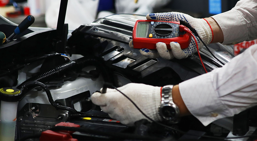 Technician using a multimeter to troubleshoot winter-related electrical issues in a truck's engine system.