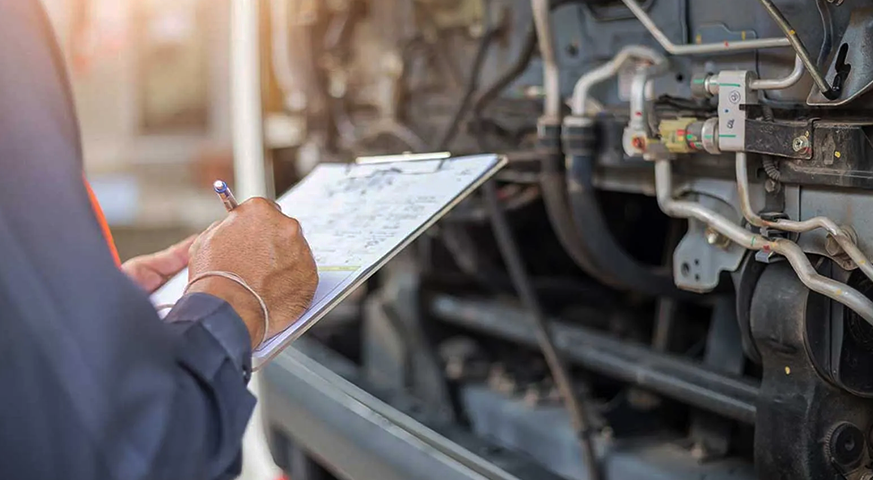 Technician conducting a preventative maintenance inspection on a long-haul truck engine with a checklist in hand.