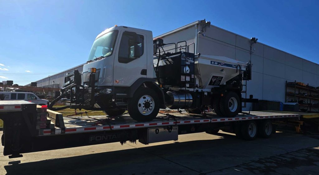 RAYCO Patcher unit weighing 18,500 lbs securely loaded on a flatbed trailer for transport from Lincolnton, NC, to West Oxford, AL