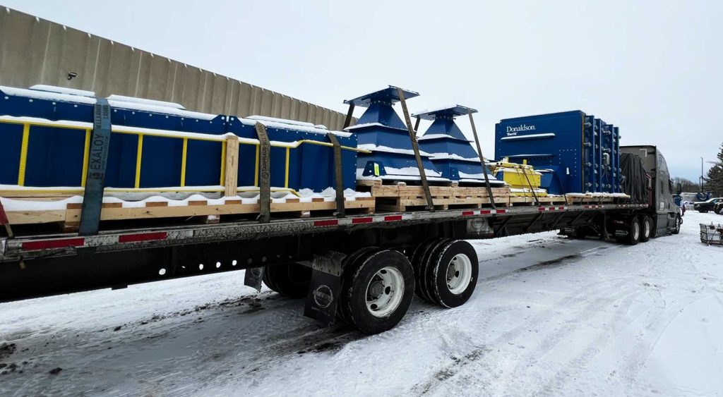 Flatbed trailer with industrial filtration equipment covered in snow, ready for delivery across state lines.