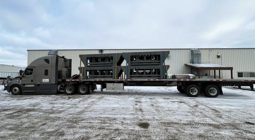 Flatbed truck carrying stacked industrial dock equipment at a snowy facility, ready for delivery to Golden, Colorado.