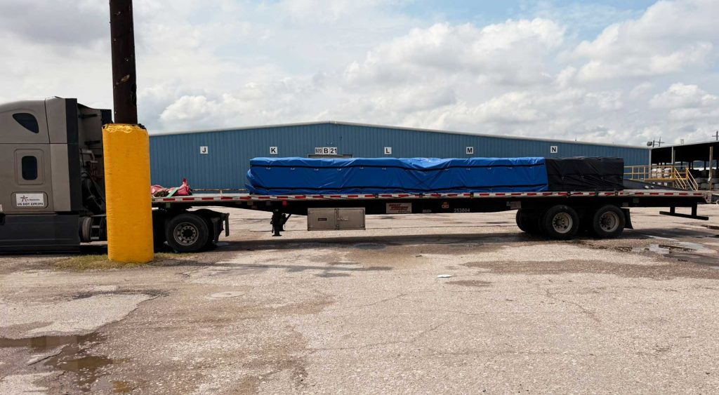 Flatbed loaded with tarped pallets at a Houston warehouse yard.