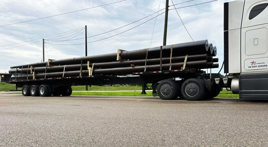 Stretch trailer hauling long ductile iron poles on the road.