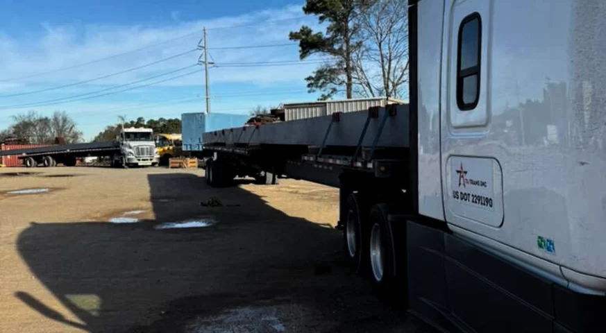 Stretch trailer loaded with a long crane girder in an industrial yard.