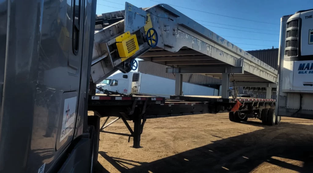 Oversize screener machine secured on an extendable flatbed trailer at a loading yard.