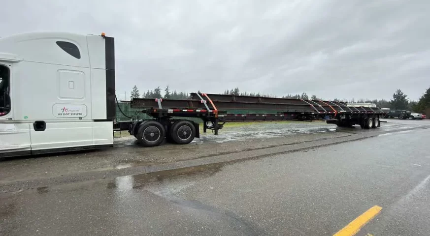 extendable flatbed trailer hauling oversized steel beams on highway flatbed trucking demand