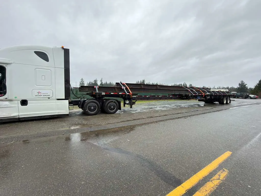 extendable flatbed trailer hauling oversized steel beams on highway flatbed trucking demand