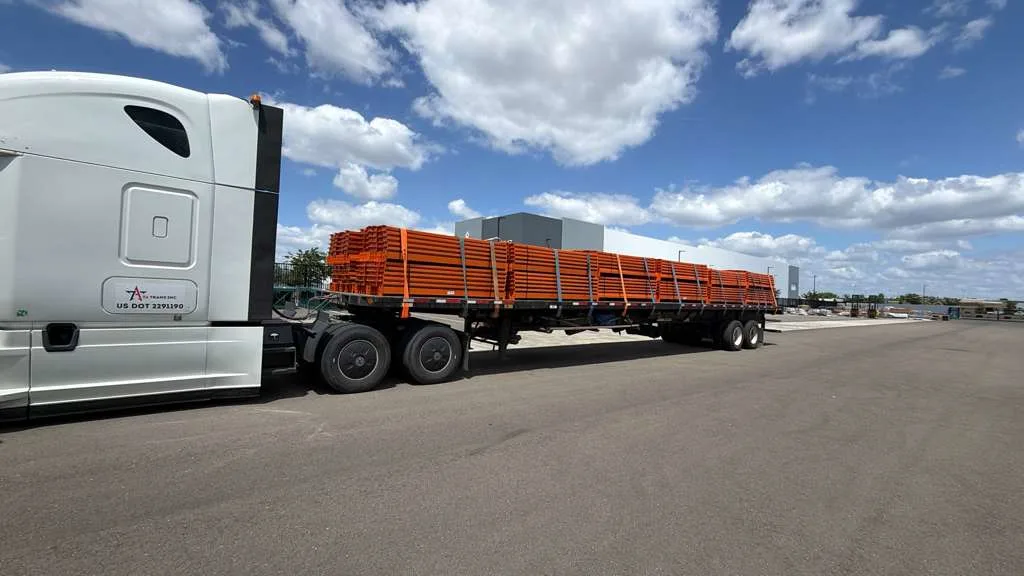 Flatbed truck hauling stacked construction materials secured with straps in an industrial area, reflecting strong freight demand contributing to higher flatbed rates in the U.S. in 2026.