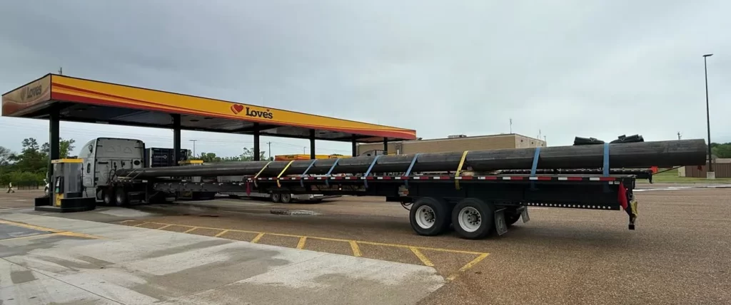 Flatbed truck hauling steel pipes parked at a Love’s truck stop in the U.S., highlighting strong construction and industrial freight demand driving higher flatbed rates in 2026.