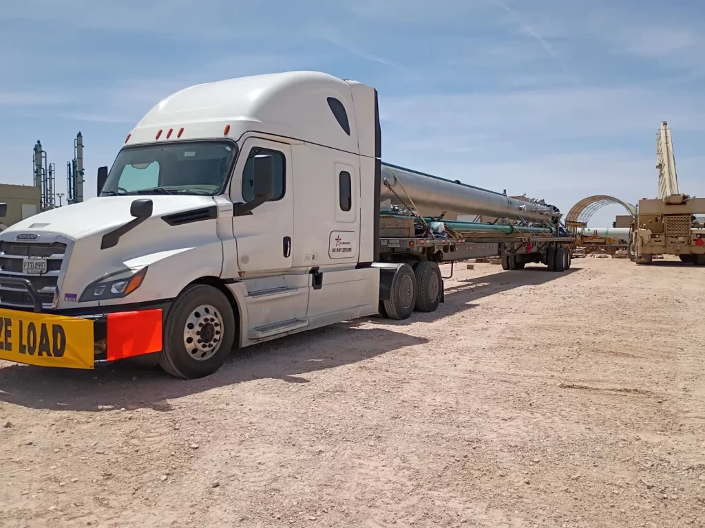 Stretch Flatbed truck hauling oversized industrial pipe at a construction site in the U.S., showing high-demand freight contributing to rising flatbed rates in 2026.