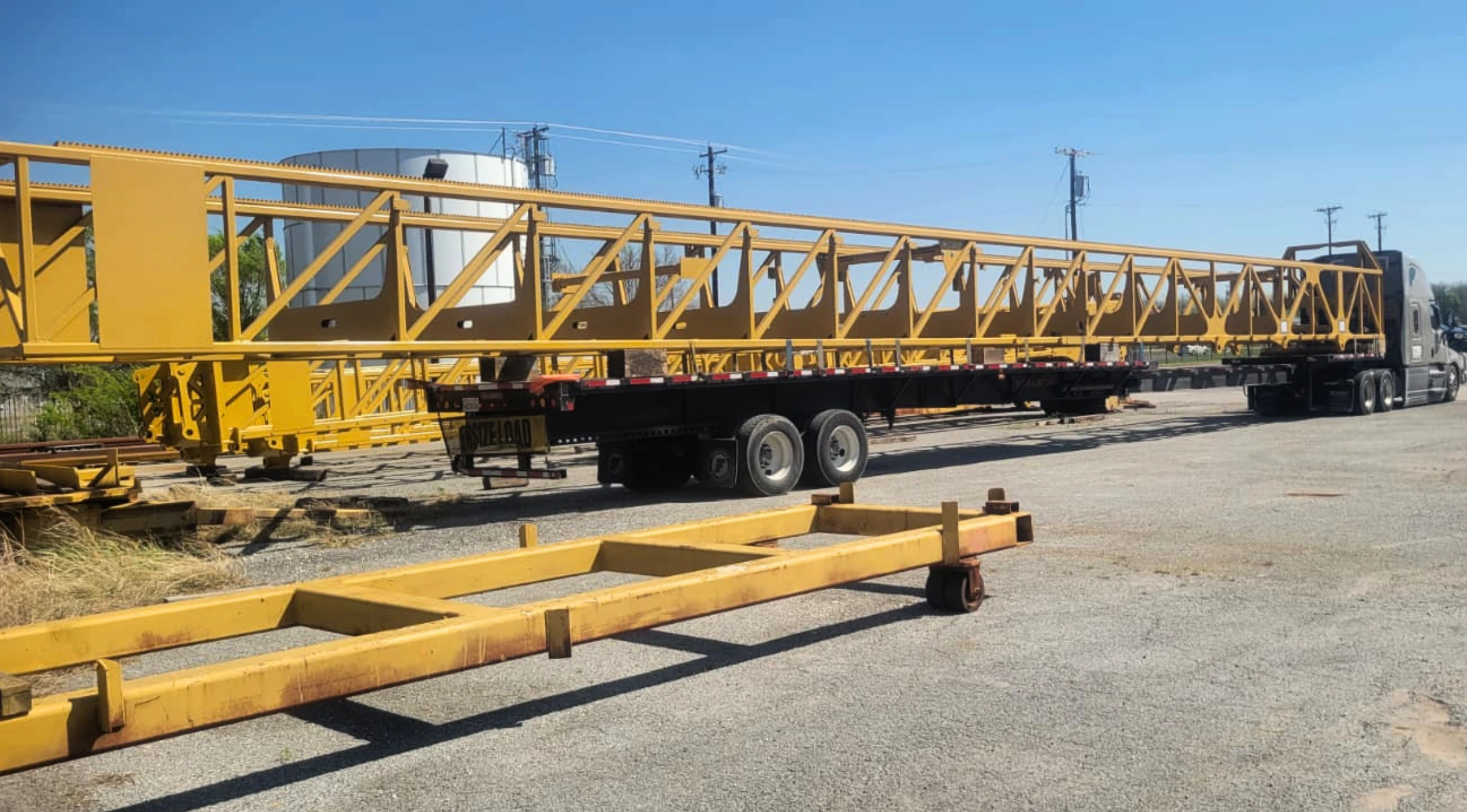 Real stretch flatbed trailer hauling a long yellow structural load in an industrial yard