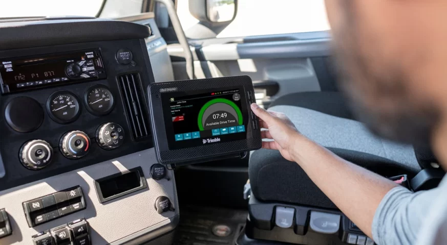 Truck driver reviewing an electronic logging device mounted inside a semi-truck cab