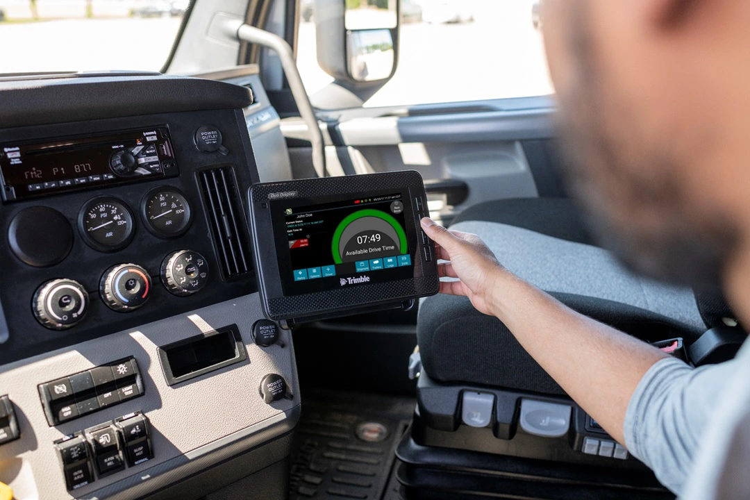 Truck driver reviewing an electronic logging device mounted inside a semi-truck cab
