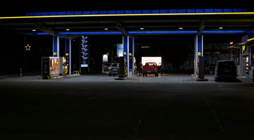 Fuel station lit at night with vehicles parked at the pumps.