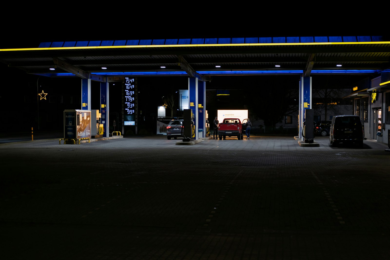 Fuel station lit at night with vehicles parked at the pumps.