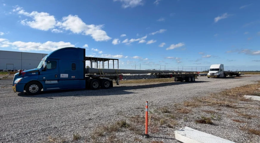 Extended flatbed trailer hauling three 75-foot utility poles from Bristol, Indiana to Fort Stockton, Texas.