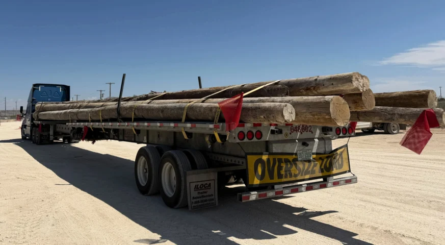 53-foot flatbed truck hauling an oversize load of wooden utility poles from McCamey, Texas to Duncan, Oklahoma.