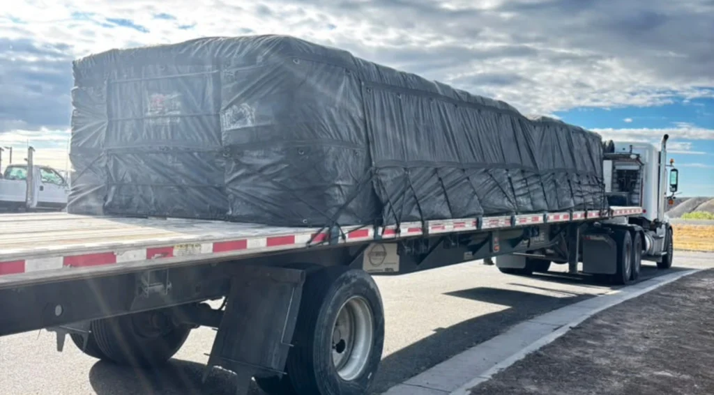 Tarped flatbed trailer carrying palletized bentonite from Greybull, Wyoming to Center, Texas.